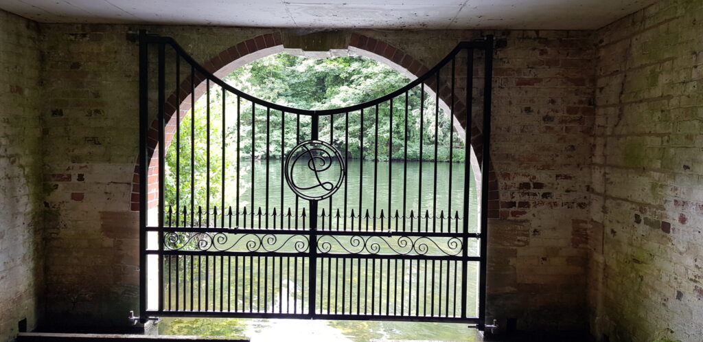 A view of the Thames through riverside gates fitted to a boat house.